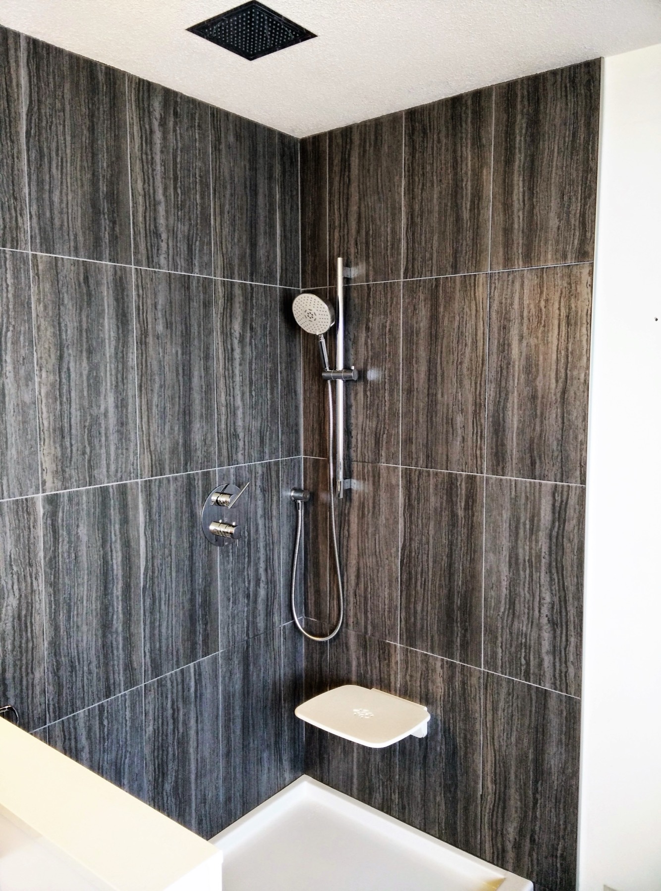 Walk in shower finished in full height dark stone tile