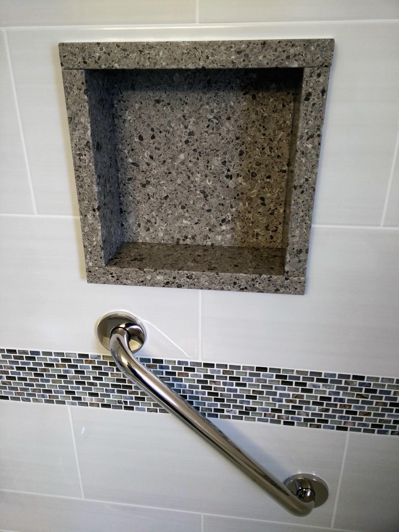 Stone shower niche with a mosaic band and a grab bar below